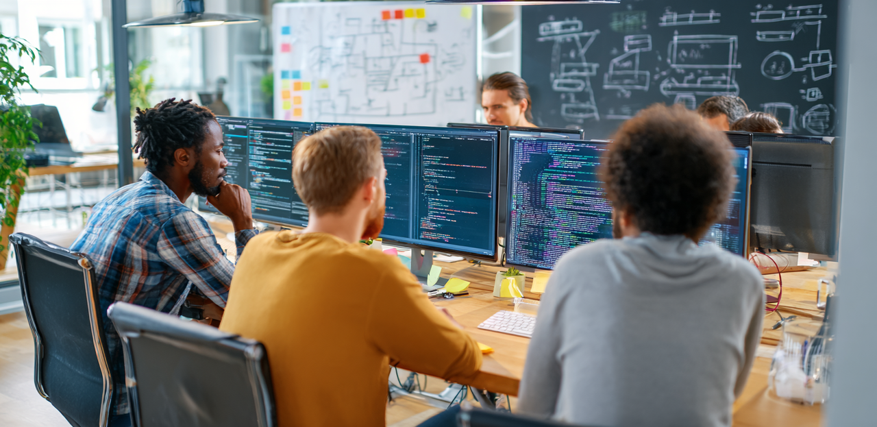 Diverse software developers collaborating on technical problems in a modern office, reviewing code and discussing solutions together